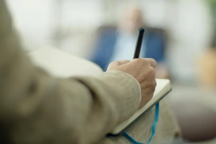 Close-up of an adult writing in a notebook with a pen, depth of field effect.