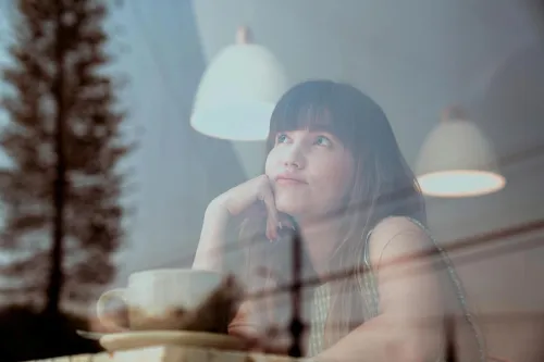 Thoughtful woman gazing outside a café window with reflections and warm lighting.