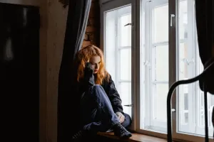 A woman sits by a window, lost in deep thoughts and moody light.
