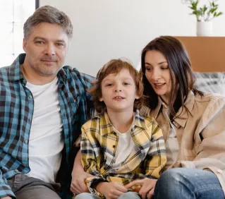 An adult couple and their child enjoying quality time at home on the couch.