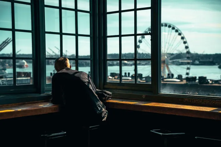 Man gazing at Seattle waterfront and ferris wheel through large windows.