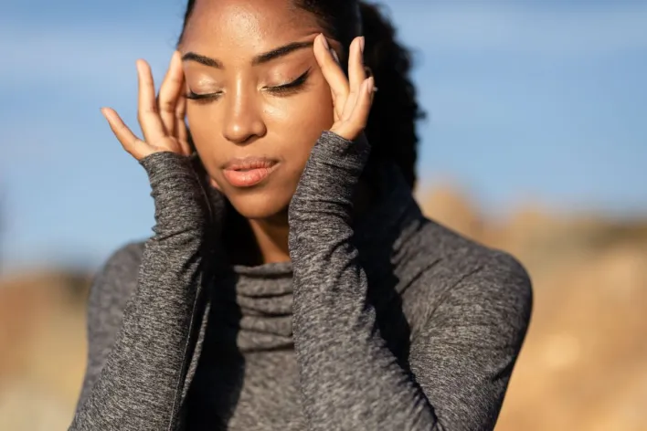 Close-up portrait of a serene woman meditating outdoors with eyes closed in sunlight.