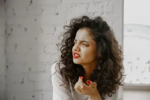 A brunette woman showing an expression of disgust against a brick wall.