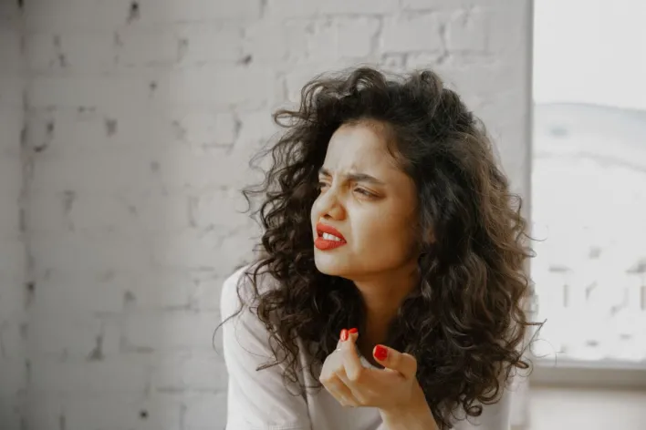A brunette woman showing an expression of disgust against a brick wall.