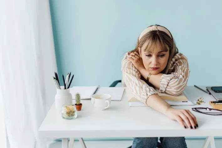 Bored woman with striped shirt at a desk with notes and coffee, reaching out.
