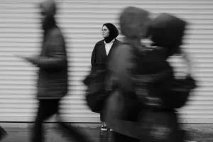 A woman in a hijab stands still amid the urban motion blur of people walking by.