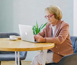 Elderly woman with glasses using a laptop at a bright, modern home interior.