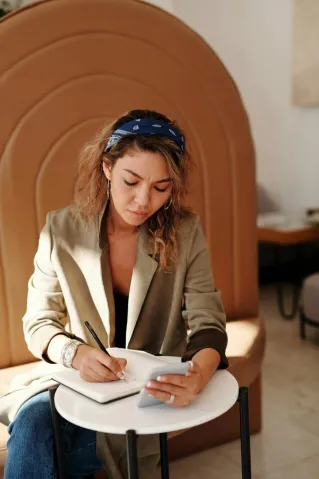 A woman jotting notes while using her smartphone in a stylish indoor setting.
