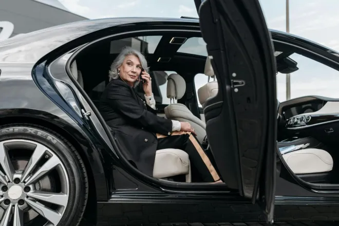 Confident senior woman sitting in a black luxury car, exuding elegance and success.