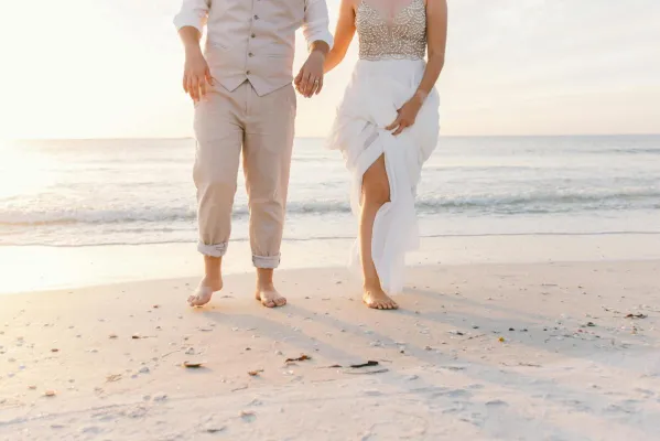 A couple walks hand in hand on a sunny beach. Perfect wedding moment captured.