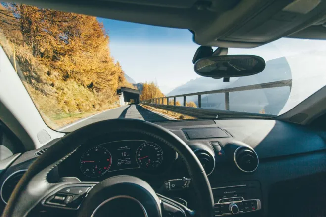 View from car interior driving through a scenic mountain road with autumn foliage and clear skies.