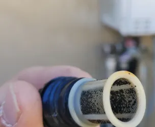 Dirty inline filter being held. Tankless heater blurred in background.