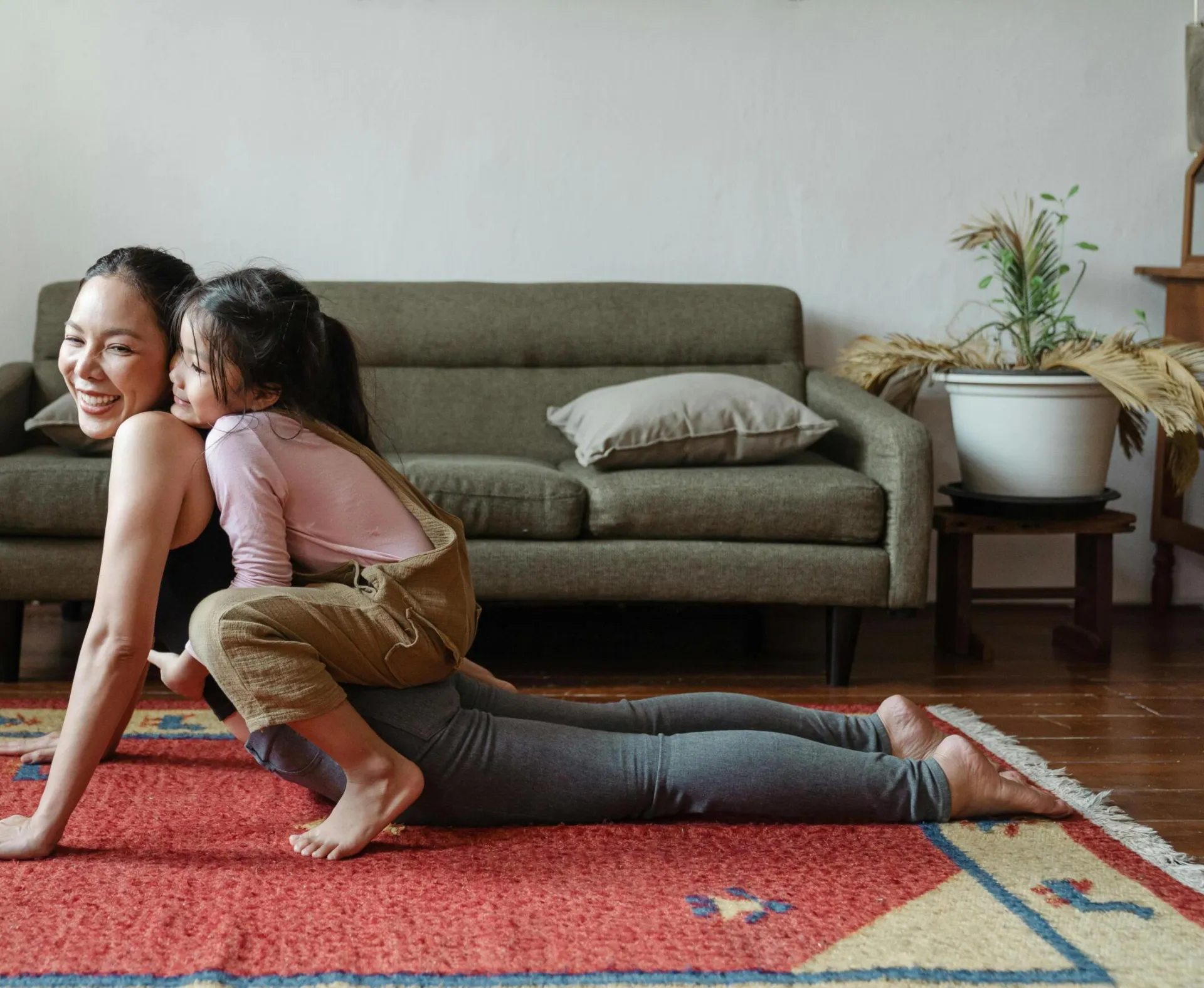 A joyful mother practicing yoga with her daughter on a colorful rug indoors.