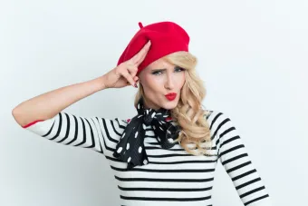 Stylish woman with red hair in a floral dress and white beret posing outdoors.