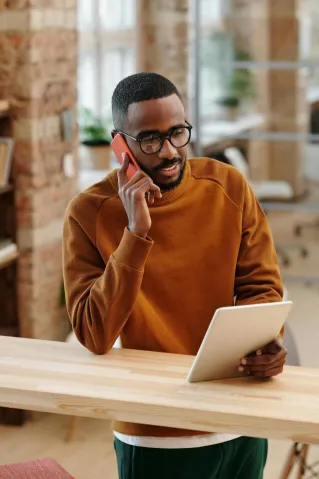 Young man in a modern office multitasking with a digital tablet and mobile phone.