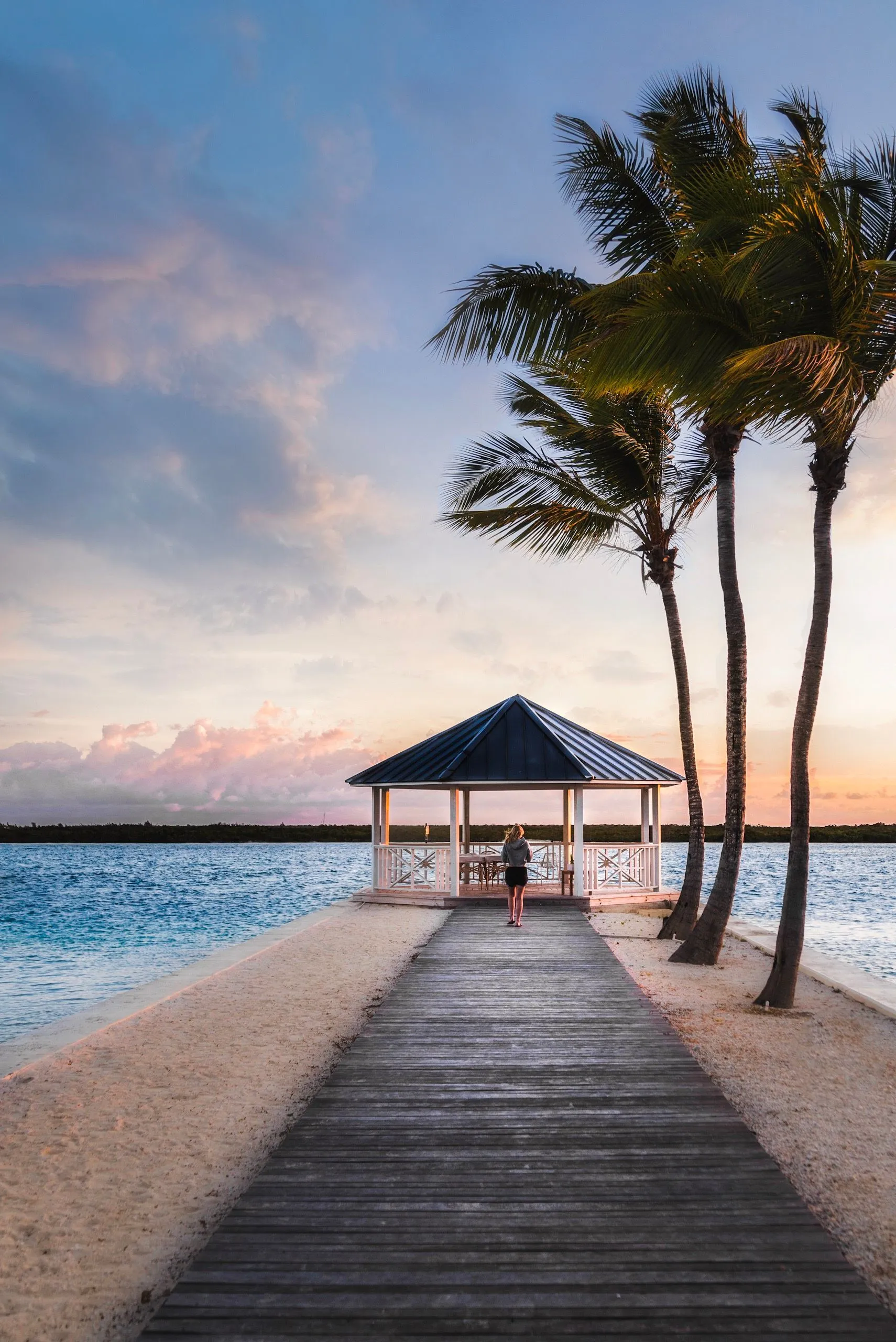 Relaxing tropical beach scene with a gazebo, palm trees, and serene sunset.