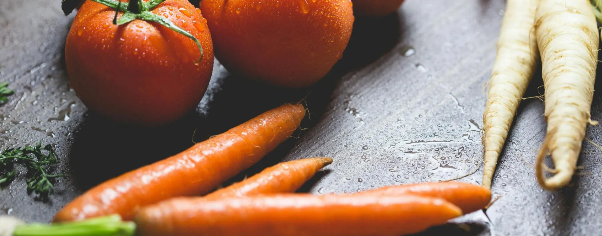 Close-up of fresh tomatoes and carrots with water droplets on a wooden surface.