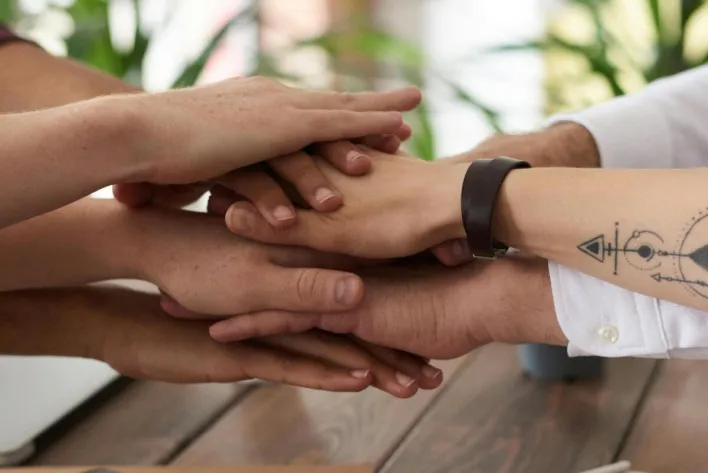 Hands from a diverse team stack on a table symbolizing unity and teamwork in a modern office setting.