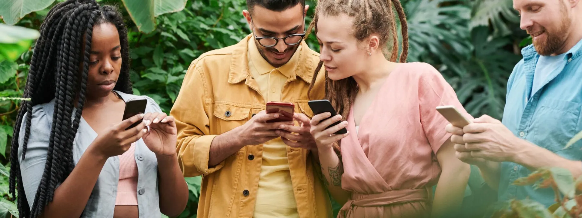 A group of young adults using smartphones in a lush outdoor setting, enjoying leisure and technology together.