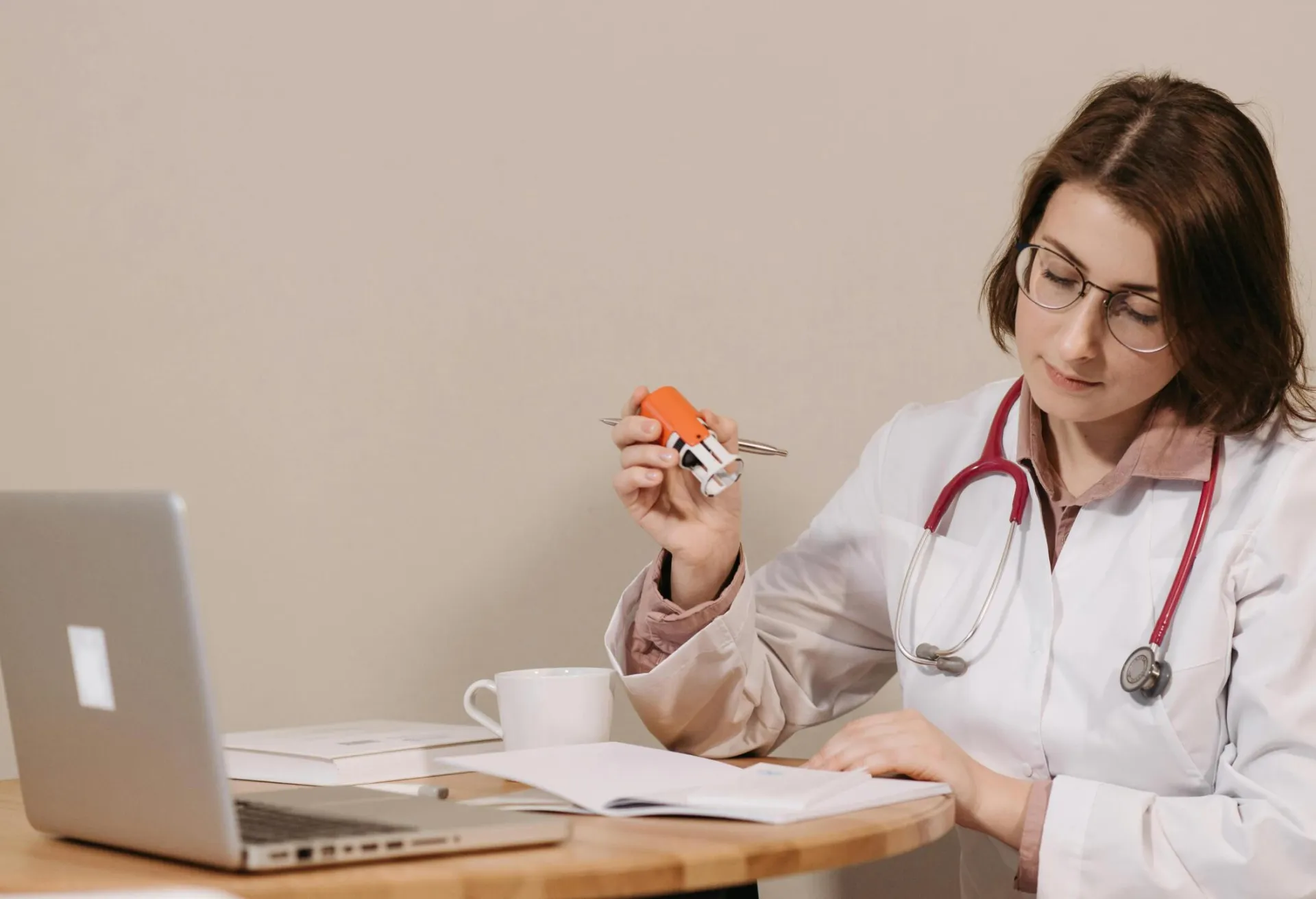 A focused female doctor reviews medical documents while sitting at her desk with a stethoscope.
