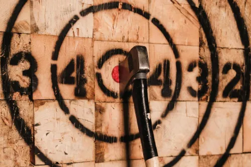 Close-up of an axe striking the bullseye on a numbered target board indoors.
