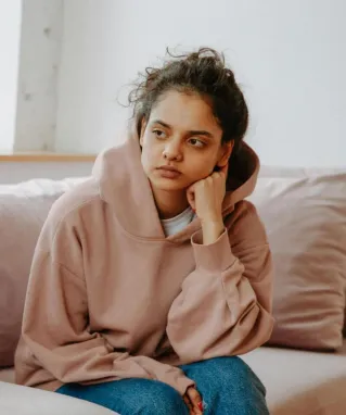 A teenager in a hoodie having a therapy session with a female therapist on a sofa.