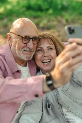 Smiling elderly couple capturing a joyful outdoor selfie moment in the park.