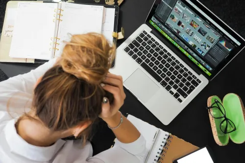 Overhead view of a stressed woman working at a desk with a laptop, phone, and notebooks.