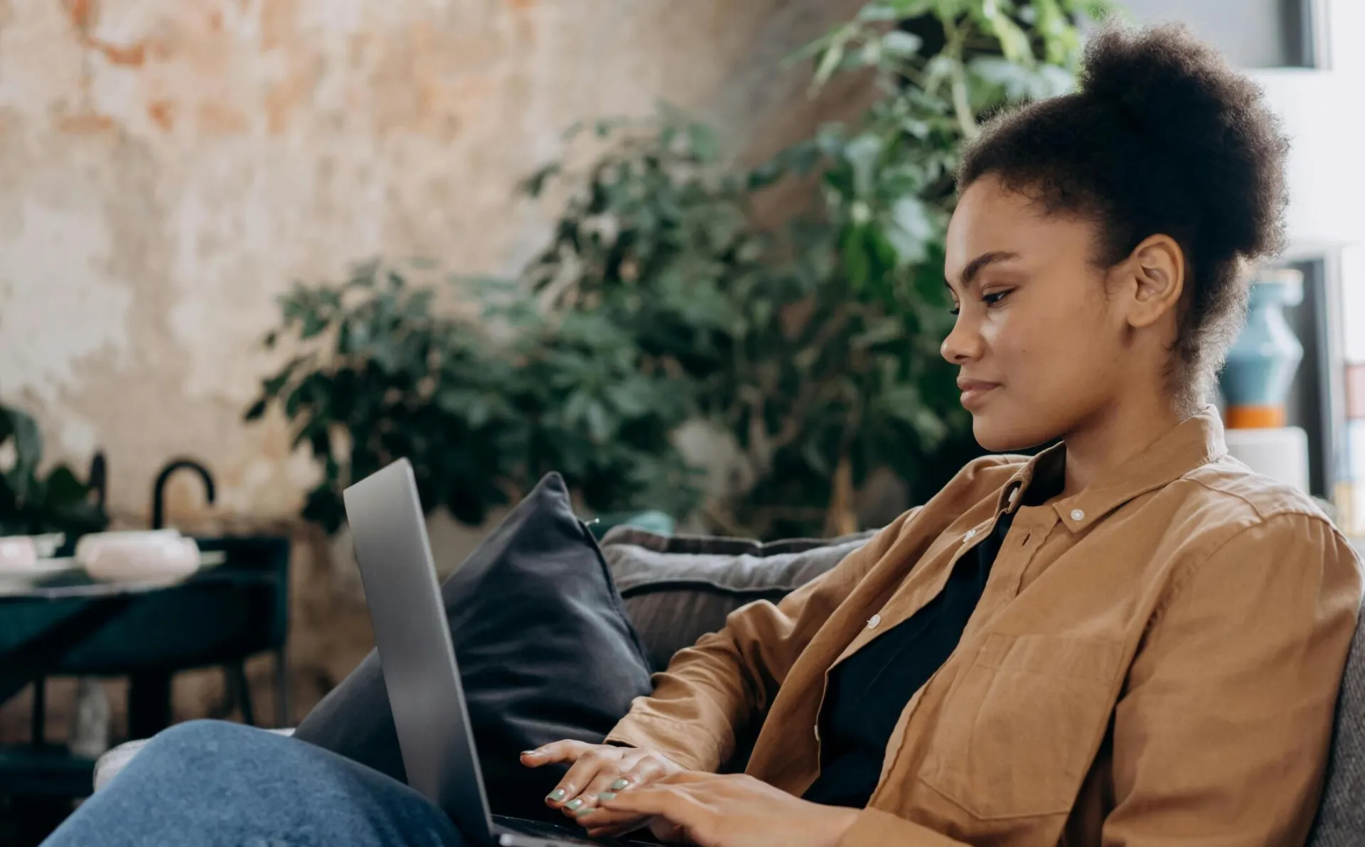 A young woman in casual clothing works on her laptop in a cozy home office setting.