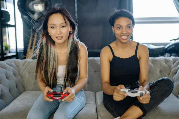 Two women playing video games on a sofa, sharing a fun leisure moment indoors.
