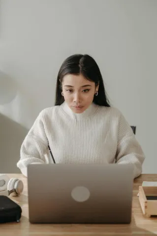 Asian woman in a cozy workspace focused on computer work, showcasing productivity in a modern setting.