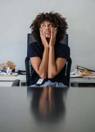 Contemplative woman in office, hands on face, expressing frustration.