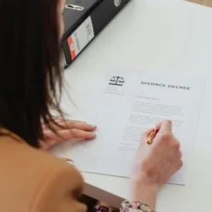 Over the shoulder view of a person signing a divorce decree at a desk in an office.