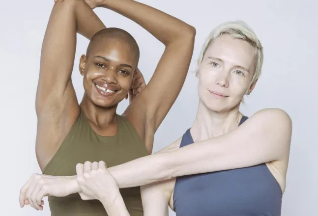 Positive diverse ladies in activewear stretching arms while standing in studio and looking at camera