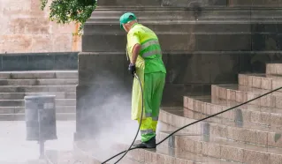 A street worker pressure washes stone stairs in a public park, ensuring cleanliness and safety.
