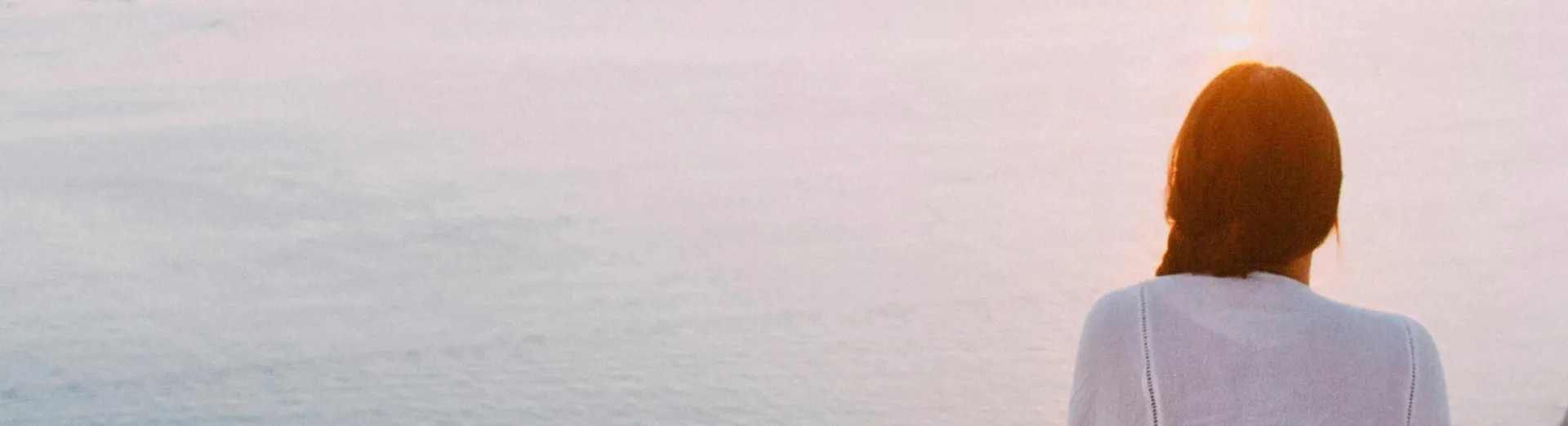 A serene view of a woman sitting on a rocky cliff, gazing at the ocean during sunset. Perfect for relaxation and travel themes.