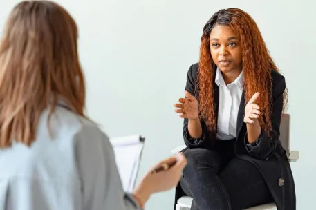 A mental health professional talking with a patient in a therapy session indoors.