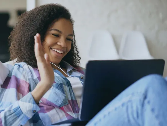 Happy woman using laptop and earphones for video call indoors.