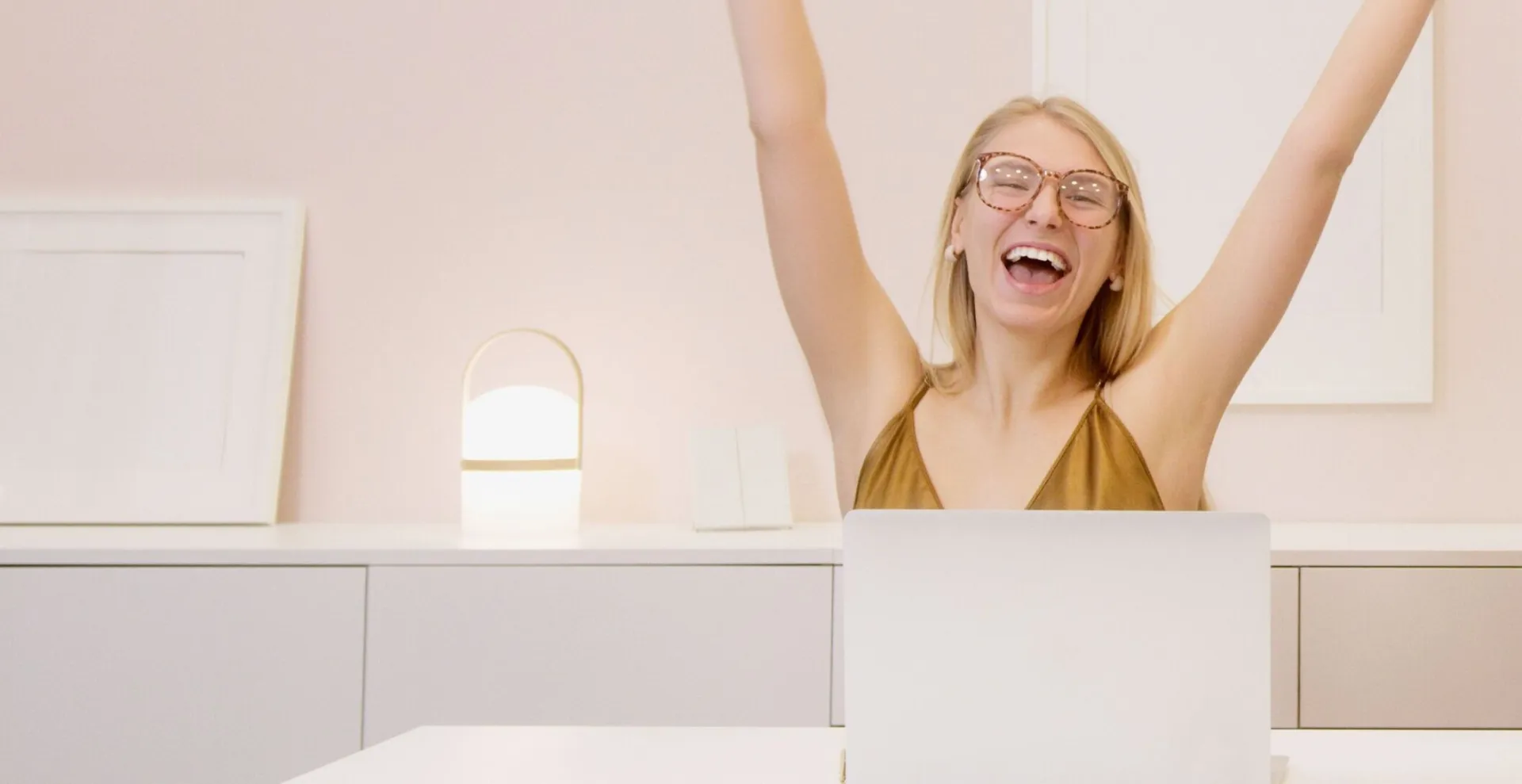 Two women celebrating a success in their modern workspace, working on laptops with blank picture frames on the wall.