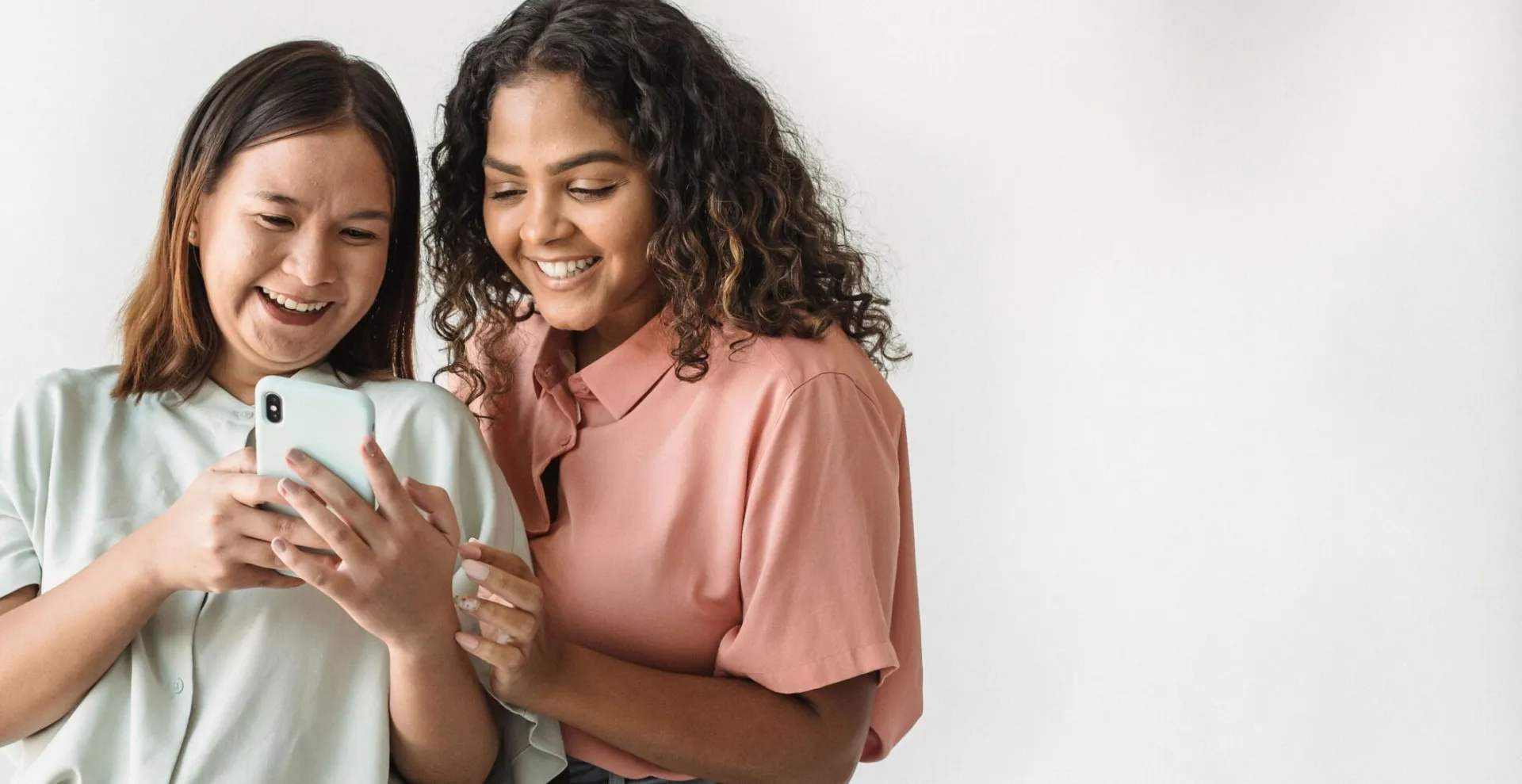 Two women smiling and looking at a smartphone together in a casual indoor setting.