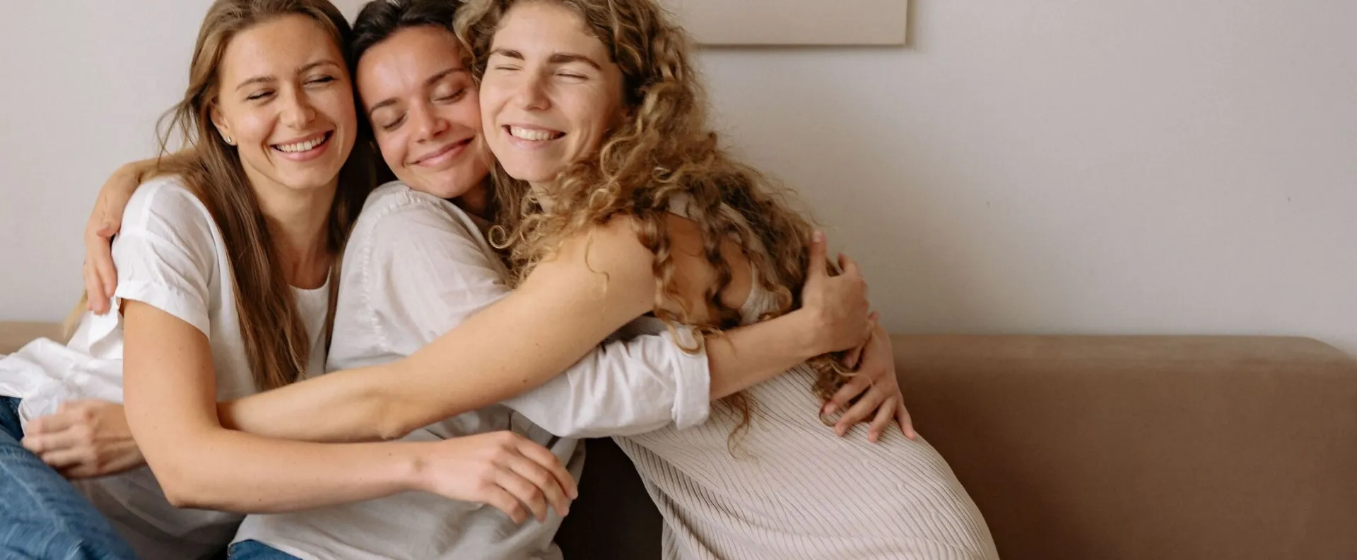 Three friends enjoy a heartfelt embrace on a cozy sofa, exuding warmth and closeness.