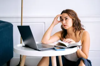 A stressed woman sitting at a desk with a laptop and notebook, reflecting work burnout.