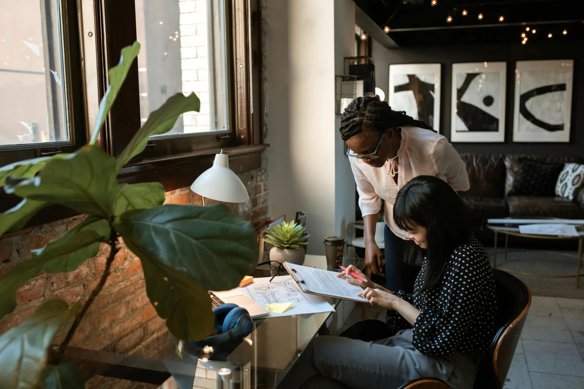 Two colleagues collaborate in a stylish, plant-filled workspace with natural light.