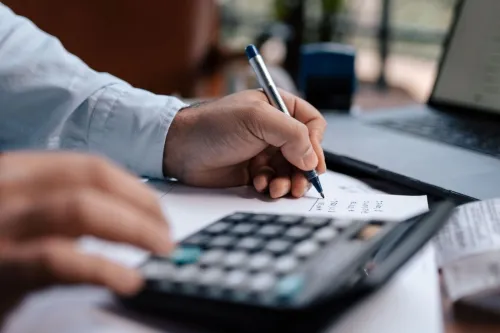 A person calculating finances with a calculator and pen on a desk indoors.