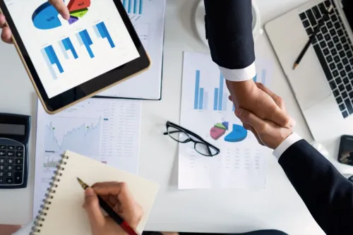 Business professionals handshake over graphs and charts in a corporate setting, symbolizing successful negotiation and agreement.