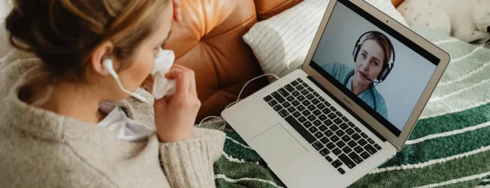 Woman having an online medical consultation on a laptop from her cozy sofa.