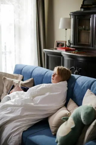 A child wrapped in a white blanket resting on a blue sofa indoors.