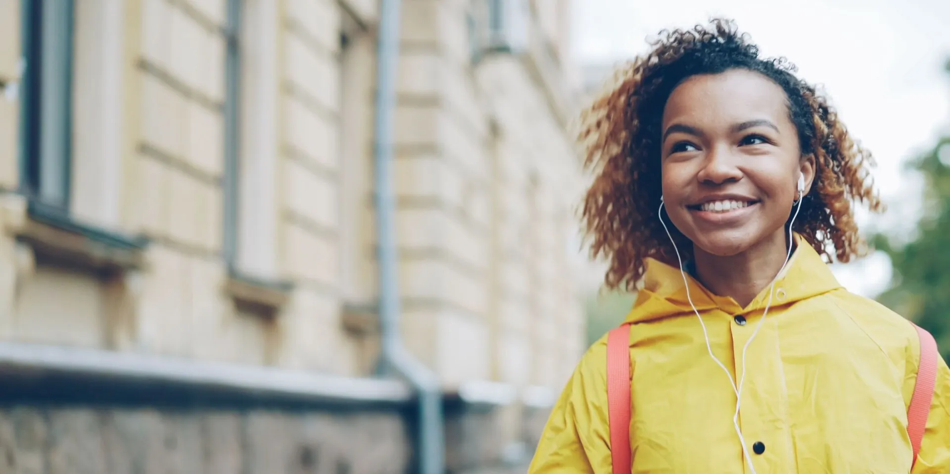 Smiling woman in yellow raincoat walking outdoors while listening to music.