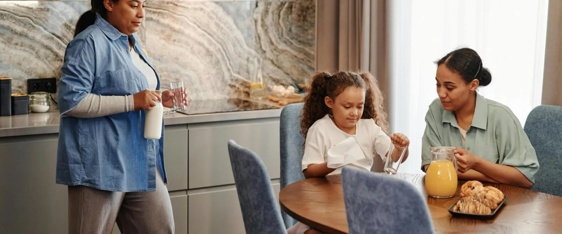 A family enjoys breakfast with pastries and drinks in a modern kitchen setting.