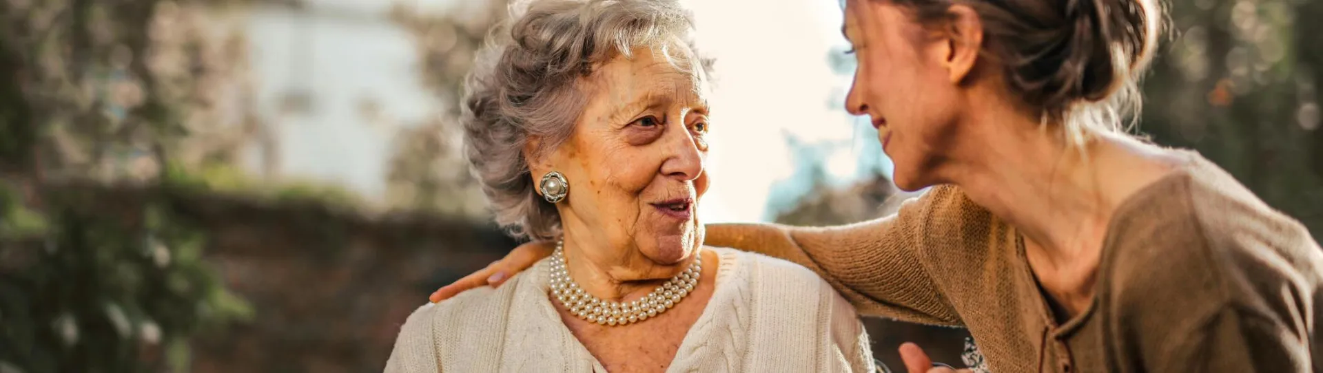 Elderly woman and adult daughter share a joyful, affectionate moment in a sunny garden.